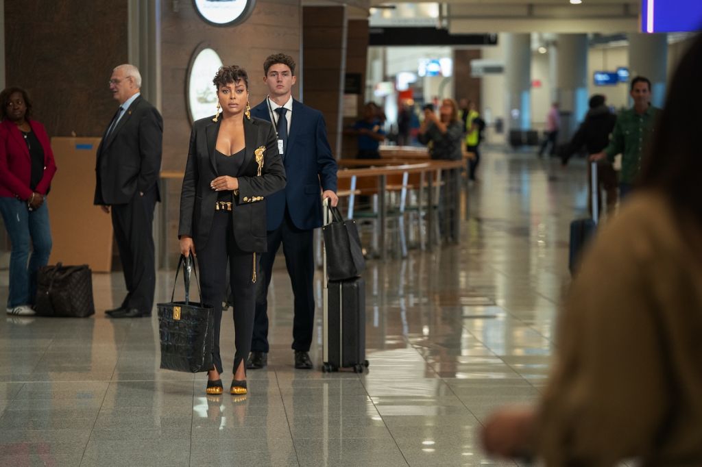 Two people, a woman and a man, walking through a busy airport terminal carrying luggage.