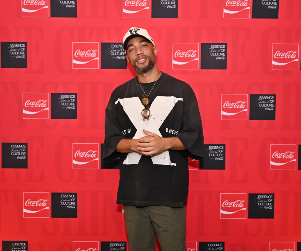 A smiling man wearing a black t-shirt with "LFG" and "BRETS" text, standing in front of a red and black Coca-Cola backdrop.