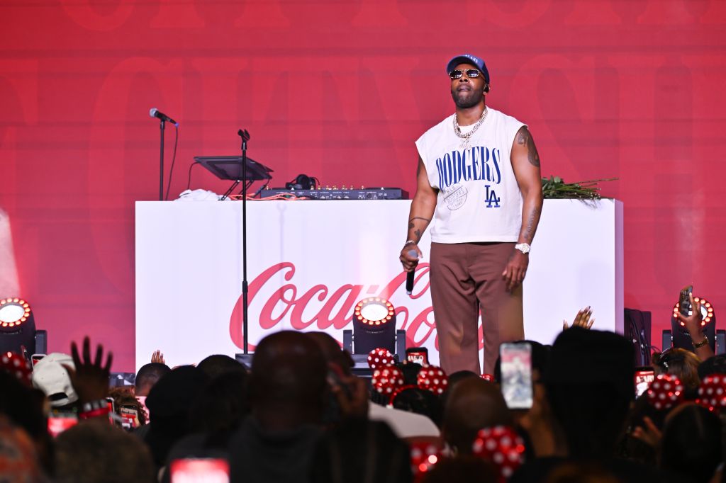 A performer wearing a "Dodgers" jersey stands on stage in front of a Coca-Cola branded backdrop, performing for a crowd.