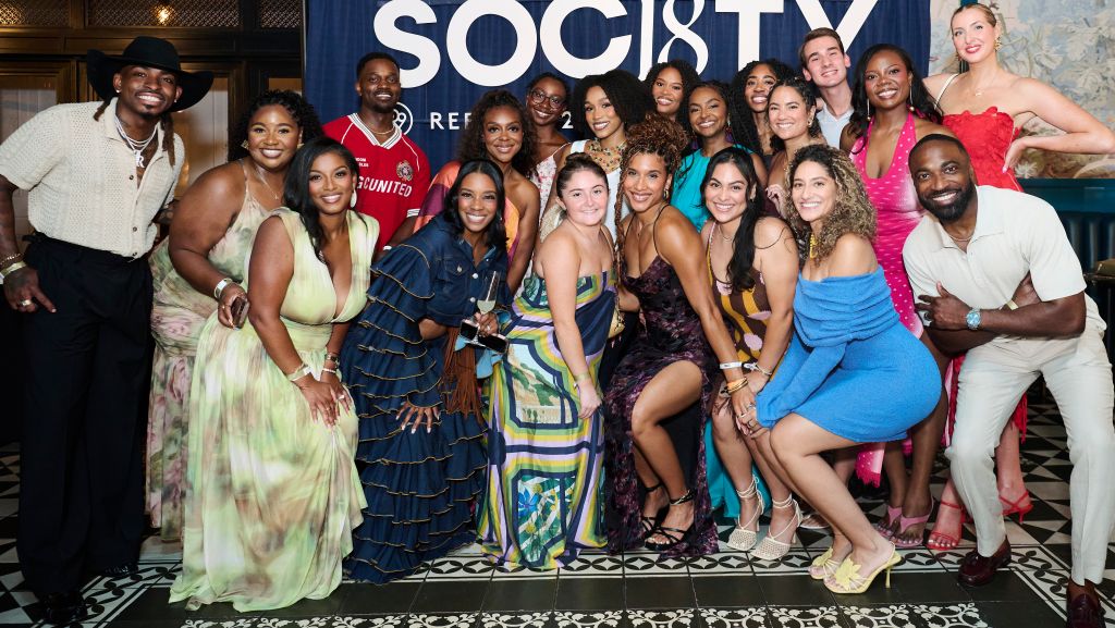 A group of diverse people posing together in front of a backdrop with the "SOCIETY" logo, some wearing formal attire and others in casual clothing.