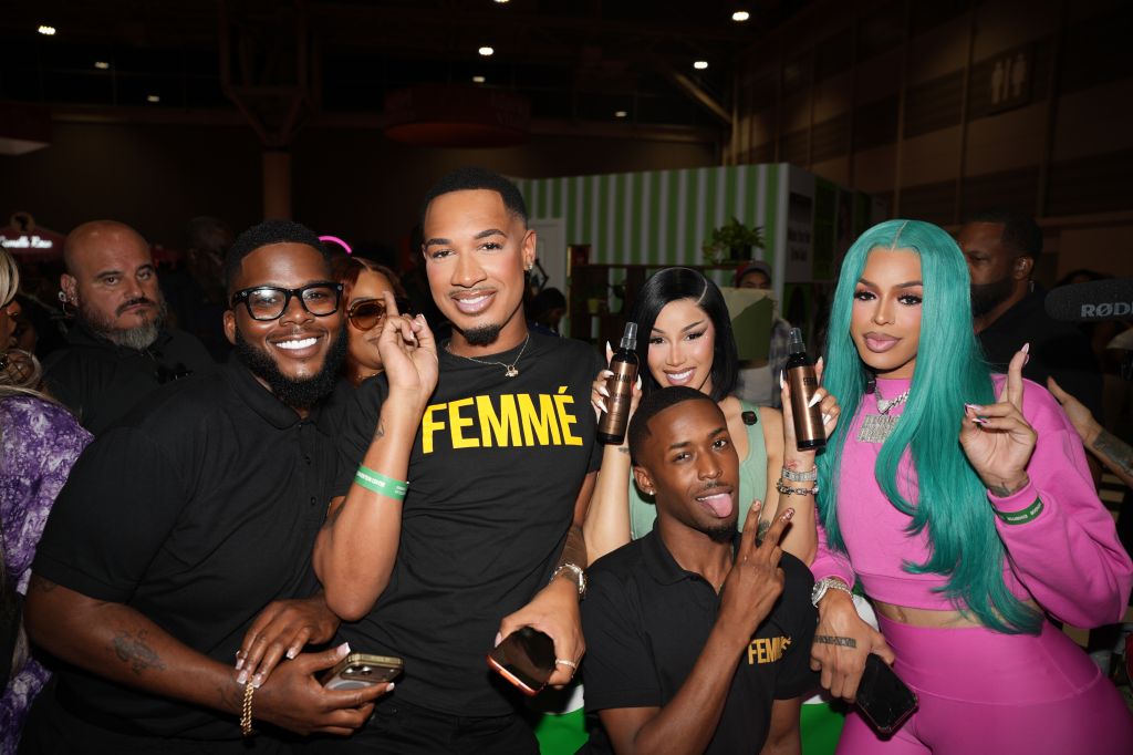 A group of people posing together, wearing clothing with the word "FEMME" printed on it, and making various hand gestures.