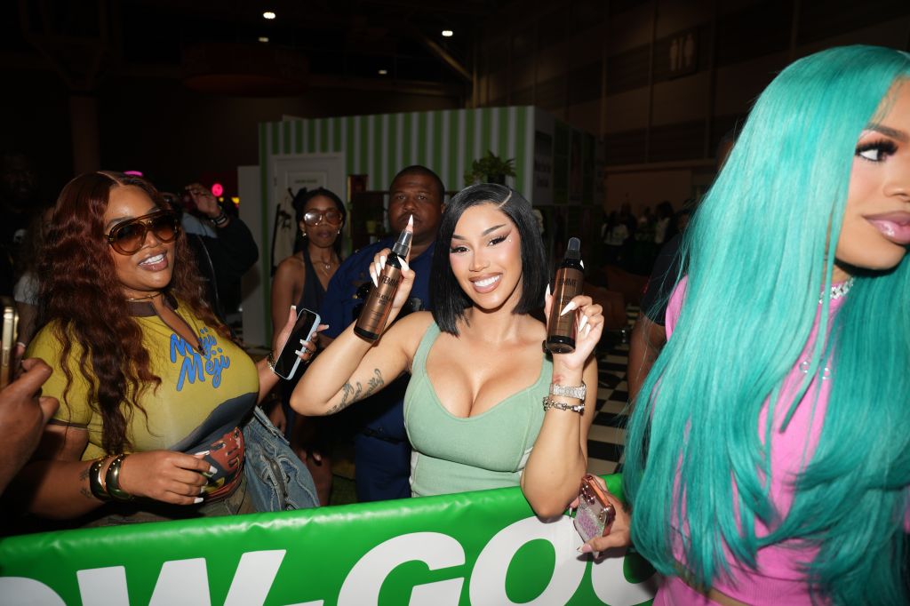 A group of people, including several women with colorful hair, holding bottles and posing in front of a green "WGOG" sign.