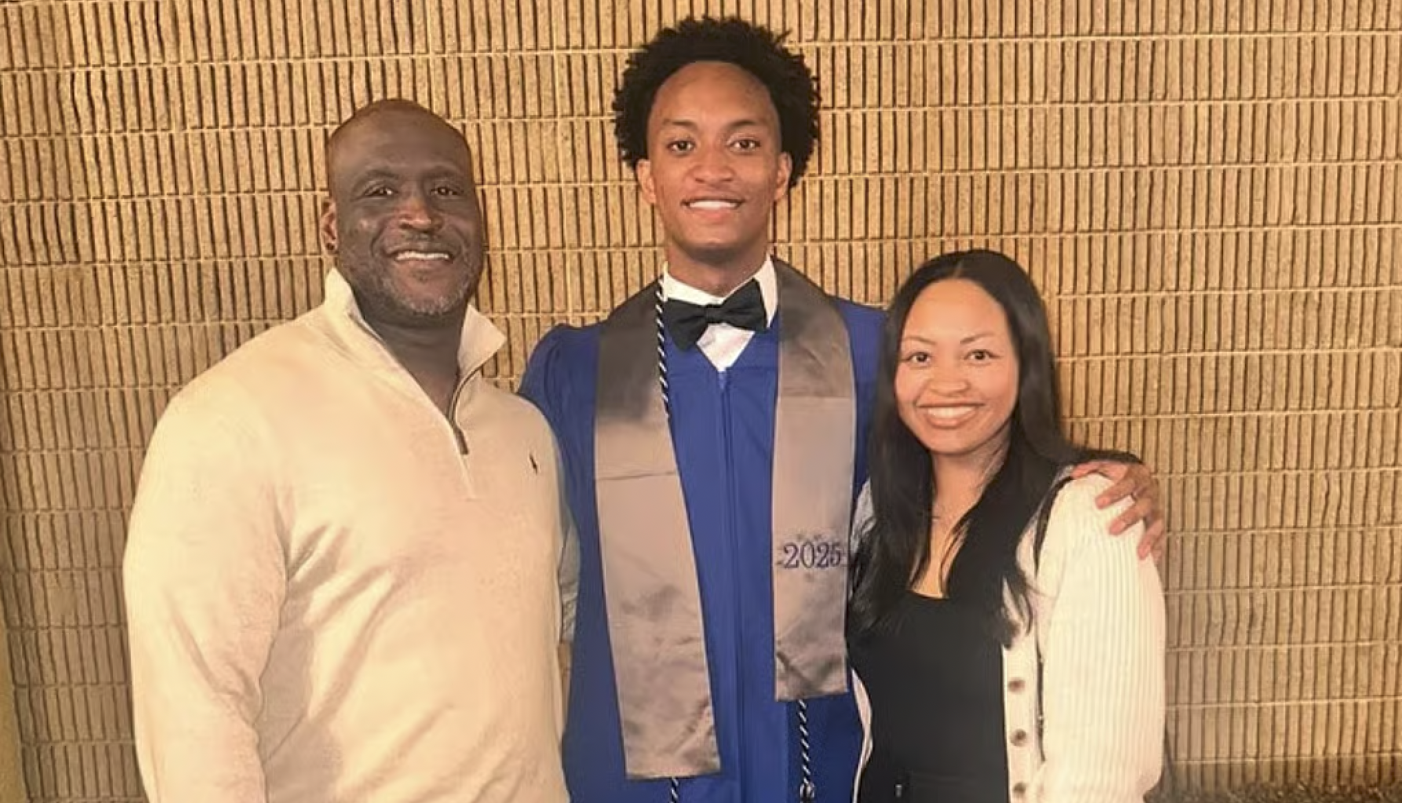 Three people posing for a photo - a man in a beige sweater, a young man in a blue graduation gown, and a woman in a white sweater.