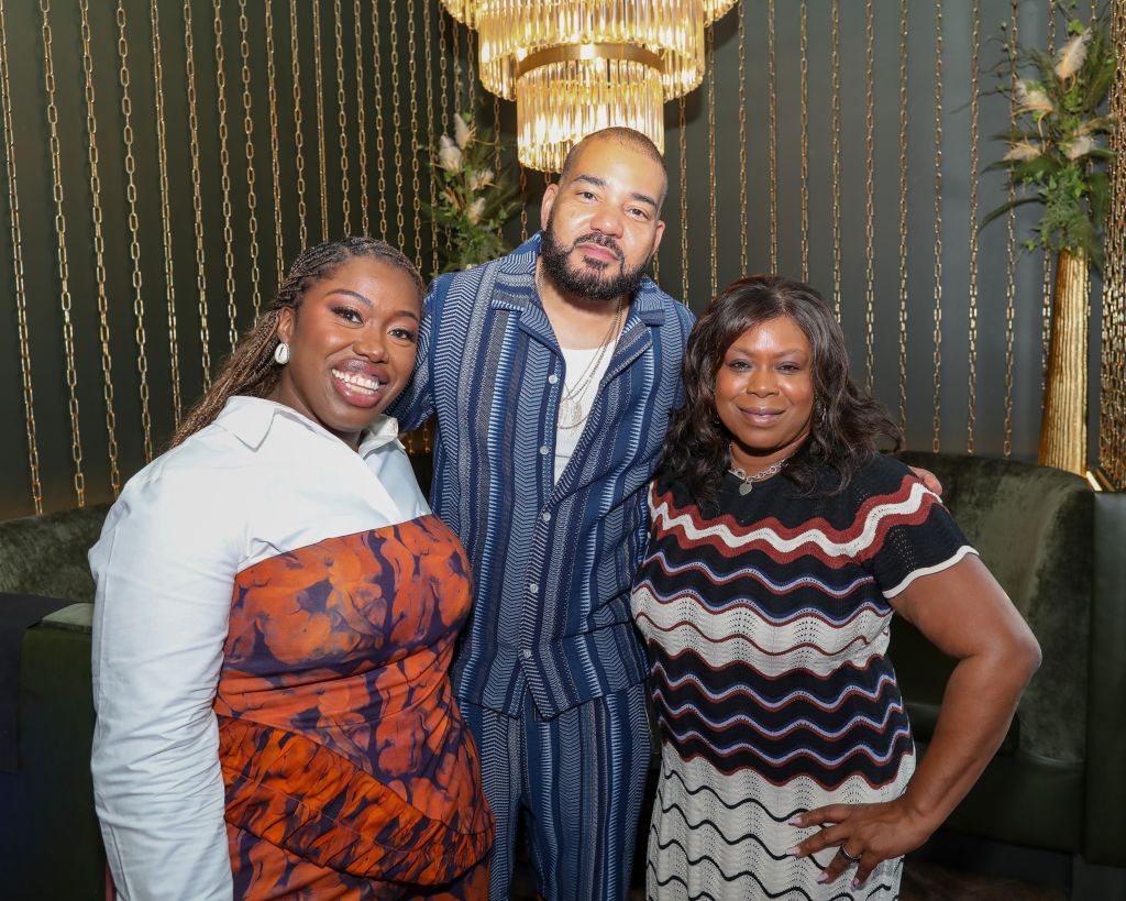 Three smiling people posing together in front of a gold chandelier.