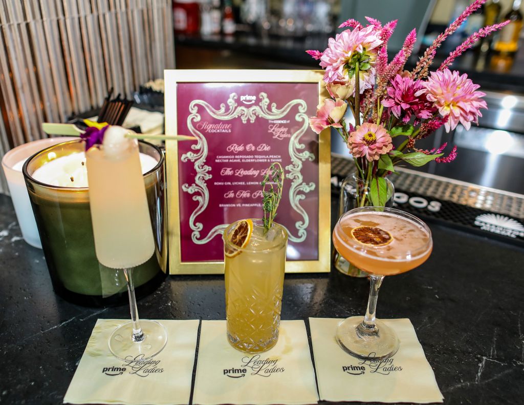 A bar display featuring a variety of cocktails and floral arrangements, with a menu board showcasing the cocktail offerings.