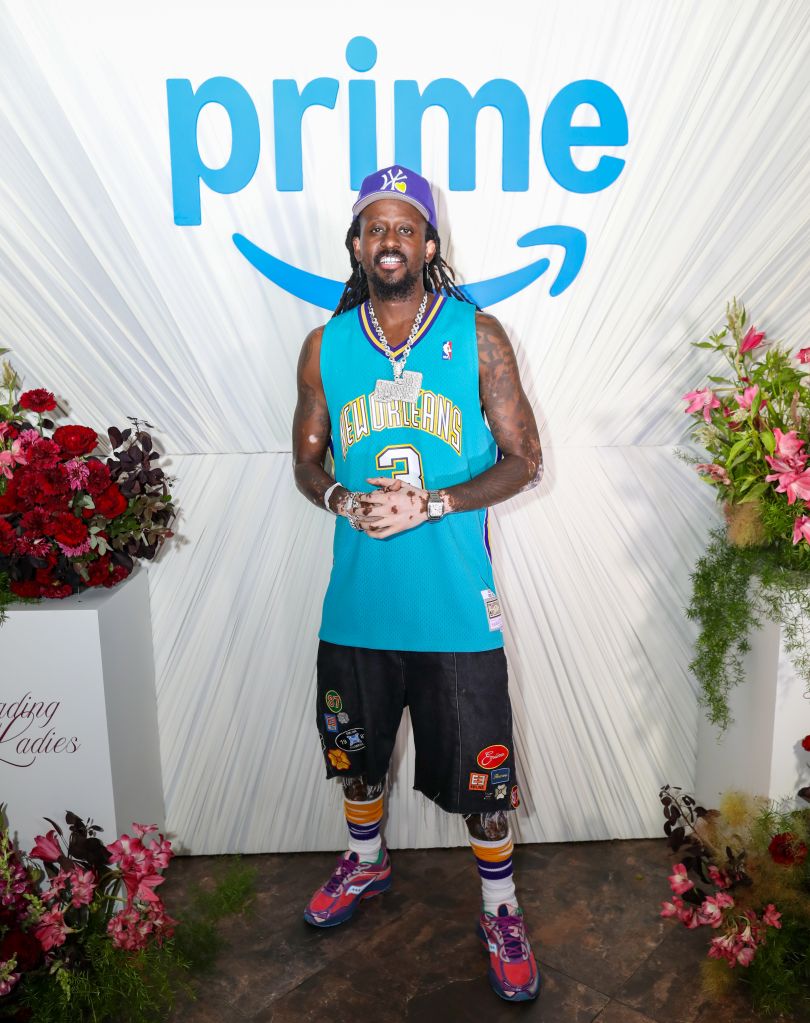 A man wearing a New Orleans Pelicans basketball jersey and accessories stands in front of a Prime logo backdrop.