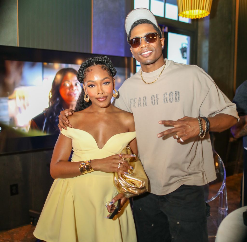 A smiling couple posing together, with the man wearing a "Year of God" t-shirt and the woman wearing a yellow off-the-shoulder dress.