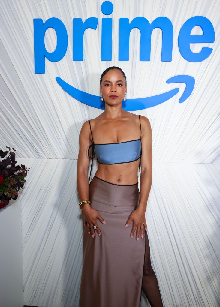 A woman wearing a blue crop top and brown skirt stands in front of a large "Prime" logo backdrop.