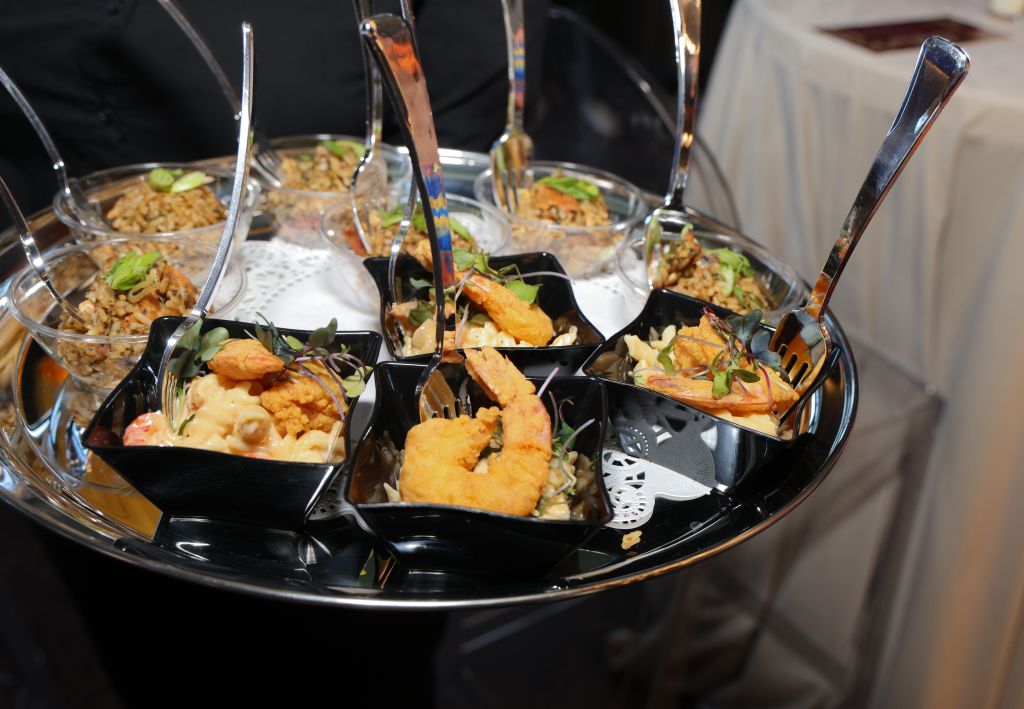 A tray of various Asian-inspired dishes, including fried items, vegetables, and grains, served in individual compartments on a black platter.