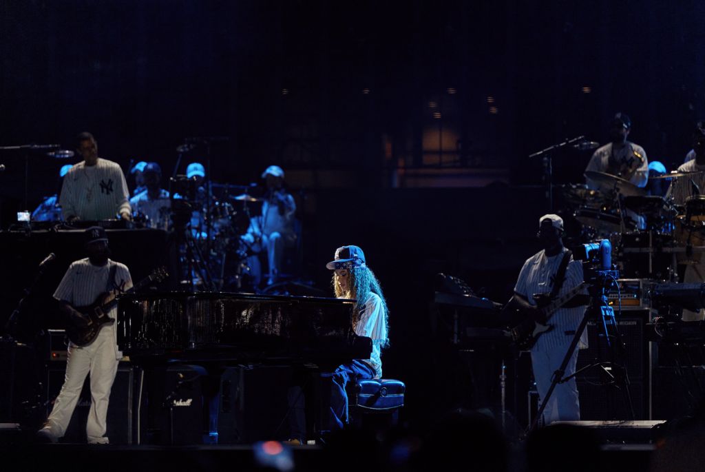 A musical performance on a dimly lit stage, with a pianist playing a grand piano and several other musicians performing on various instruments.