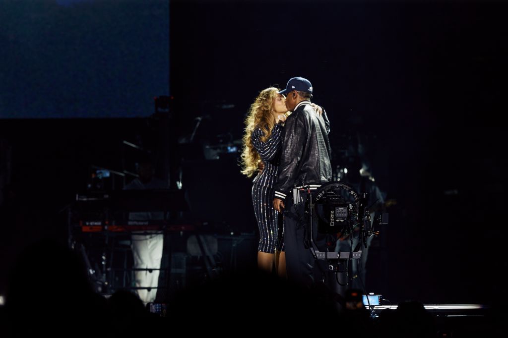 Two people embracing on a dark stage with musical equipment visible in the background.