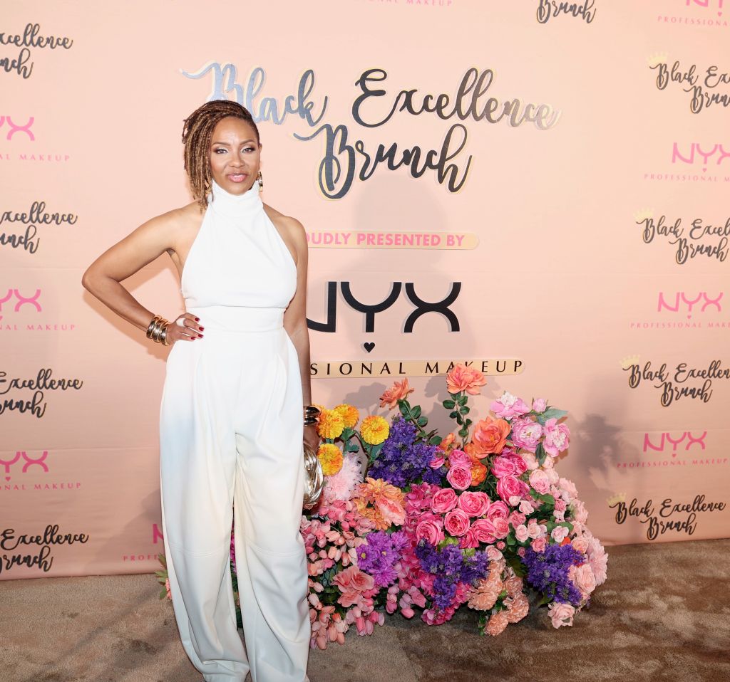 A woman in a white jumpsuit posing in front of a backdrop with the text "Black Excellence Brunch" and the NYX Professional Makeup logo.