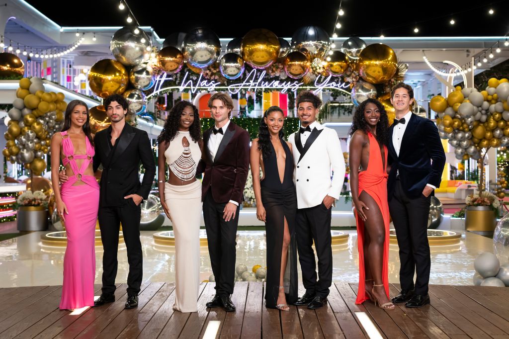 A group of well-dressed people posing in front of a festive backdrop with gold and silver balloons and the text "It was always you".
