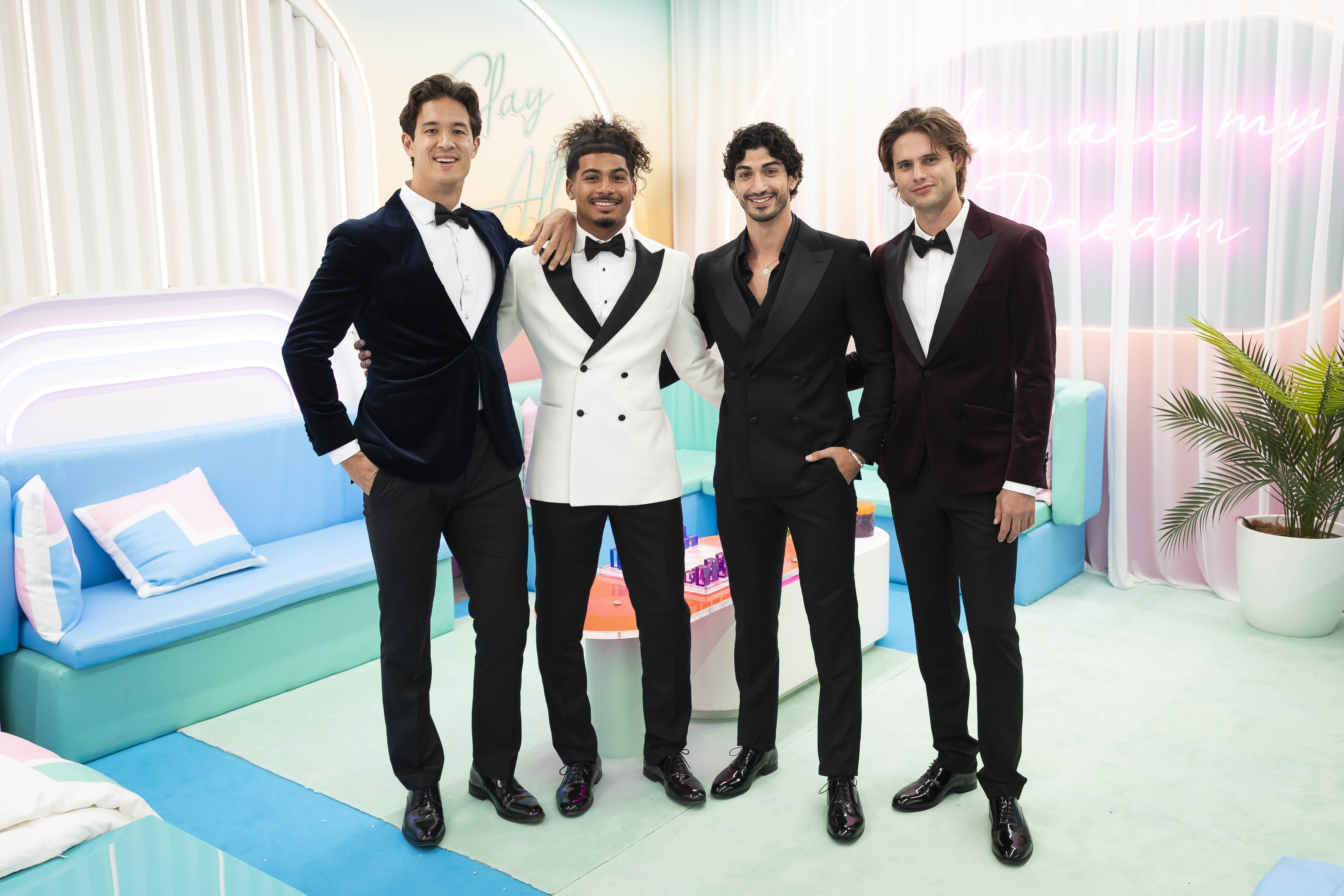 Four well-dressed young men posing together in a colorful, modern setting.