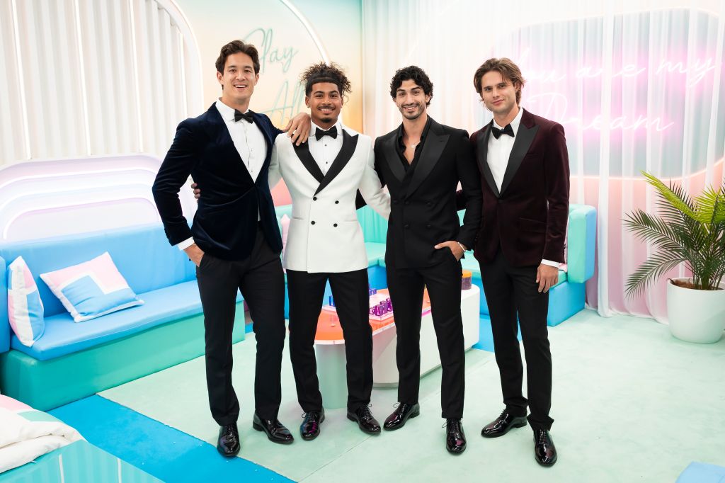 Four well-dressed young men posing together in a colorful, modern setting.