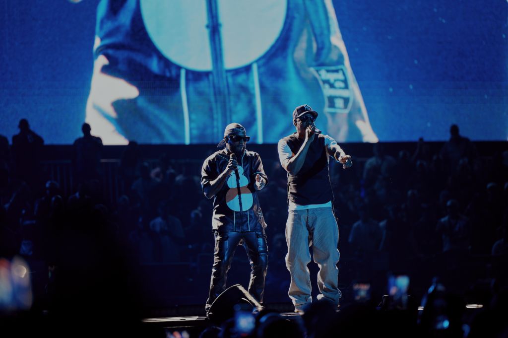 Two performers on stage in front of a large screen displaying a blue and white graphic design.