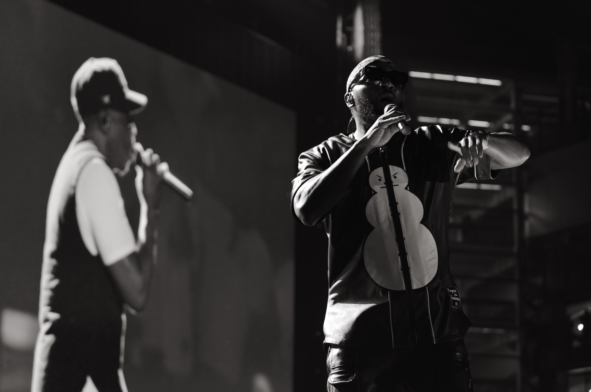 Two musicians performing on stage, one playing an electric guitar and the other singing into a microphone.