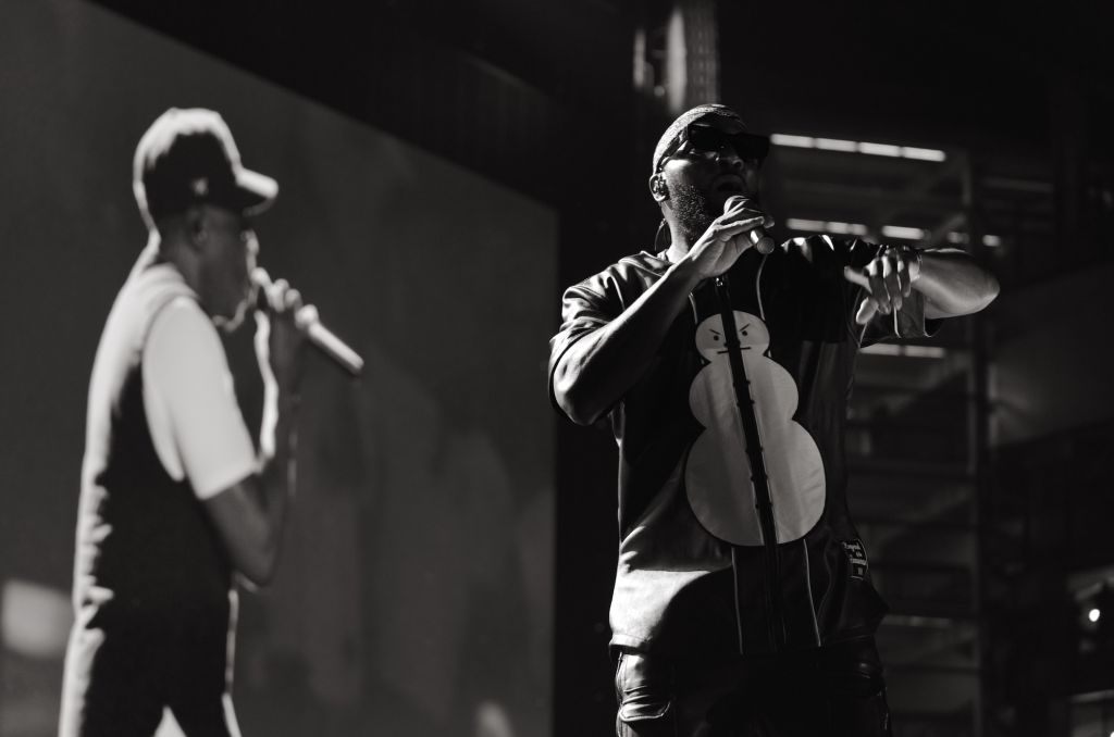 Two musicians performing on stage, one playing an electric guitar and the other singing into a microphone.