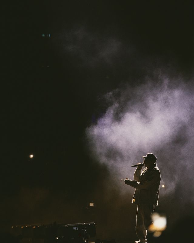 A silhouetted figure performing on a dimly lit stage, surrounded by smoke and atmospheric lighting.