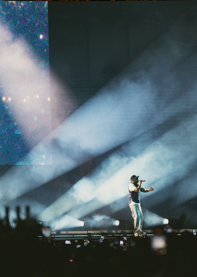 A performer on stage surrounded by smoke and lights, holding a microphone and singing.