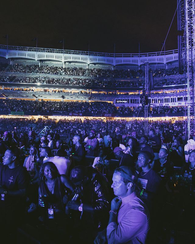 A large crowd of people gathered in a sports stadium at night, with bright lights and signage visible.