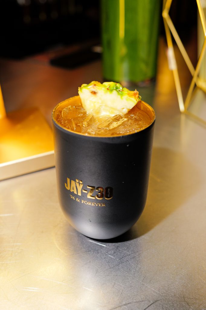 A black cup with the text "JAY-230 '96 & FOREVER" filled with a yellow, icy drink garnished with a lemon slice.