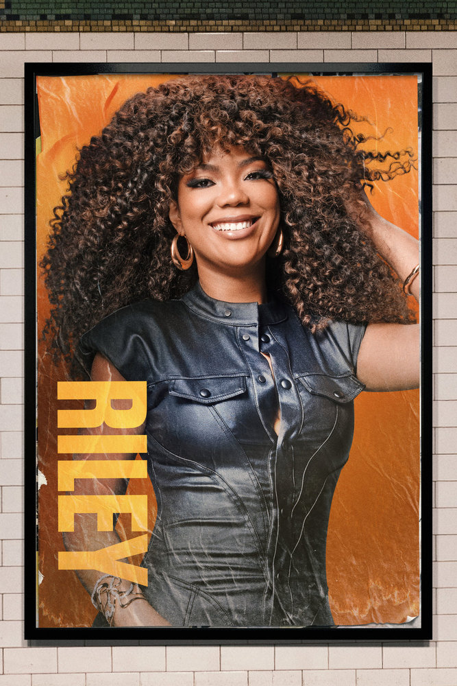 A smiling woman with curly brown hair wearing a black leather jacket stands against an orange background with the text "RILEY" in large yellow letters.