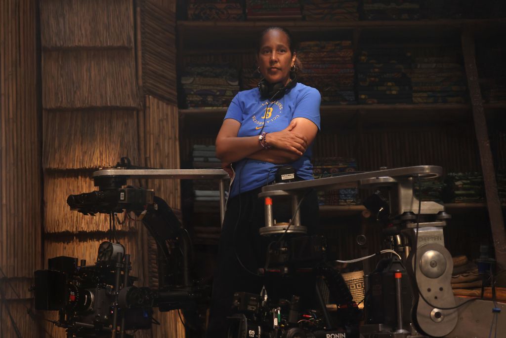 A woman in a blue shirt stands with her arms crossed in a room full of film equipment.