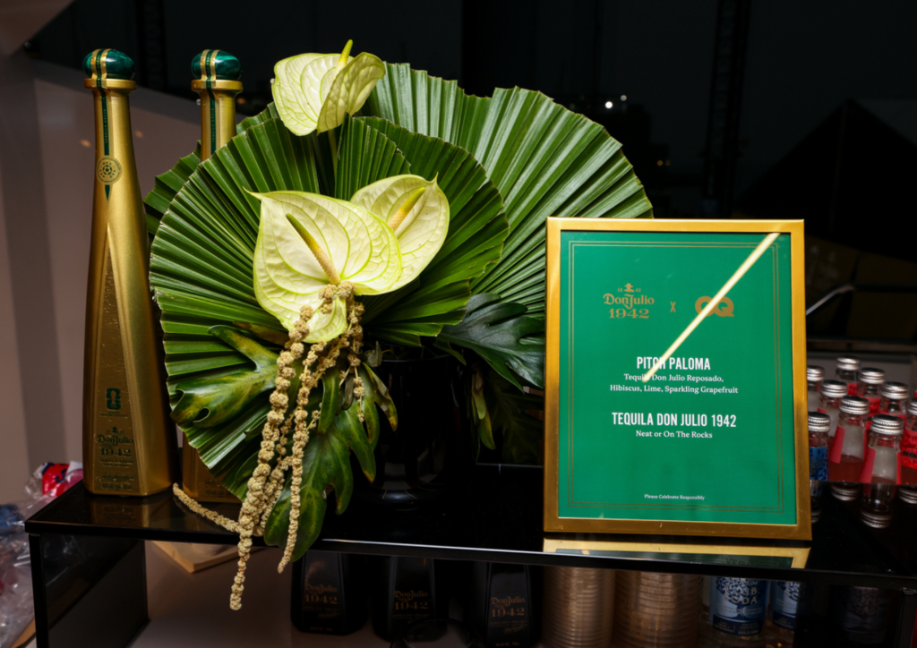 A display of tropical flowers and leaves, including anthurium and palm fronds, alongside bottles of Tequila Don Julio 1942 and a framed advertisement for the "Pitch Paloma" cocktail.