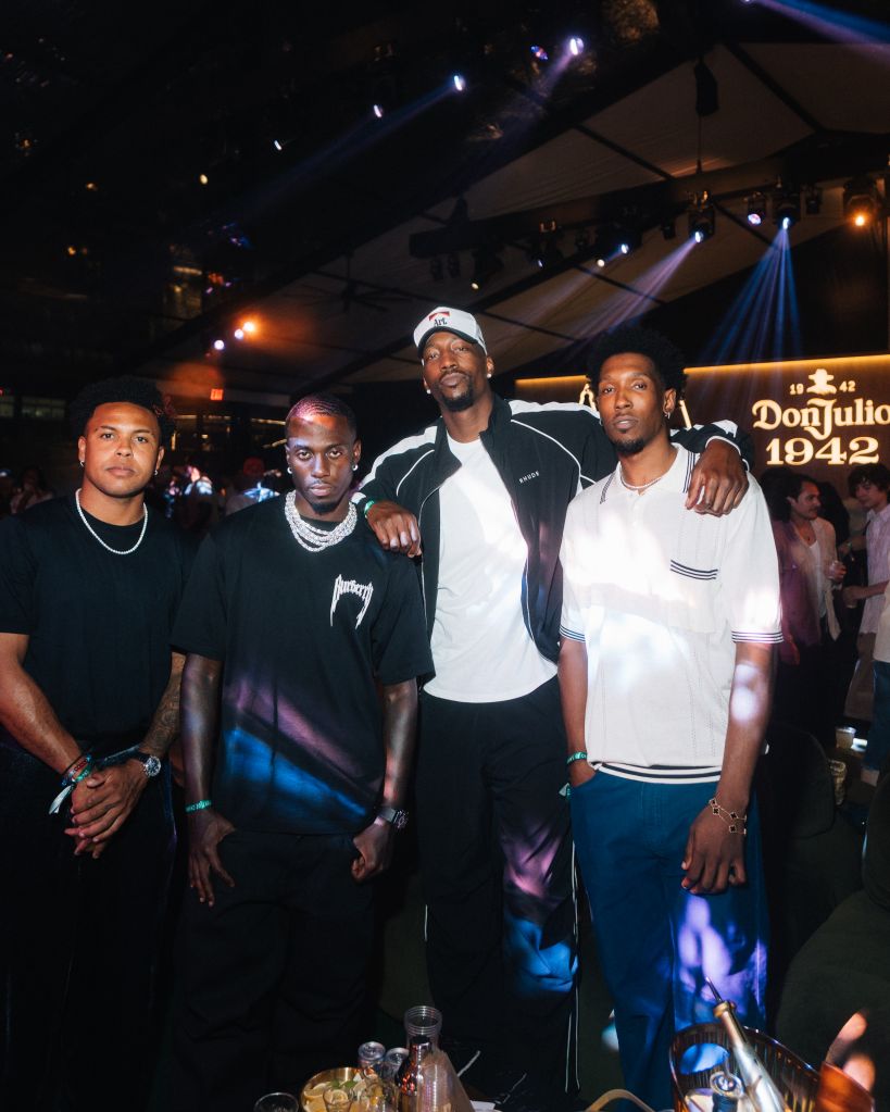Four men standing together in a nightclub setting, with a "Don Julio 1942" sign visible in the background.