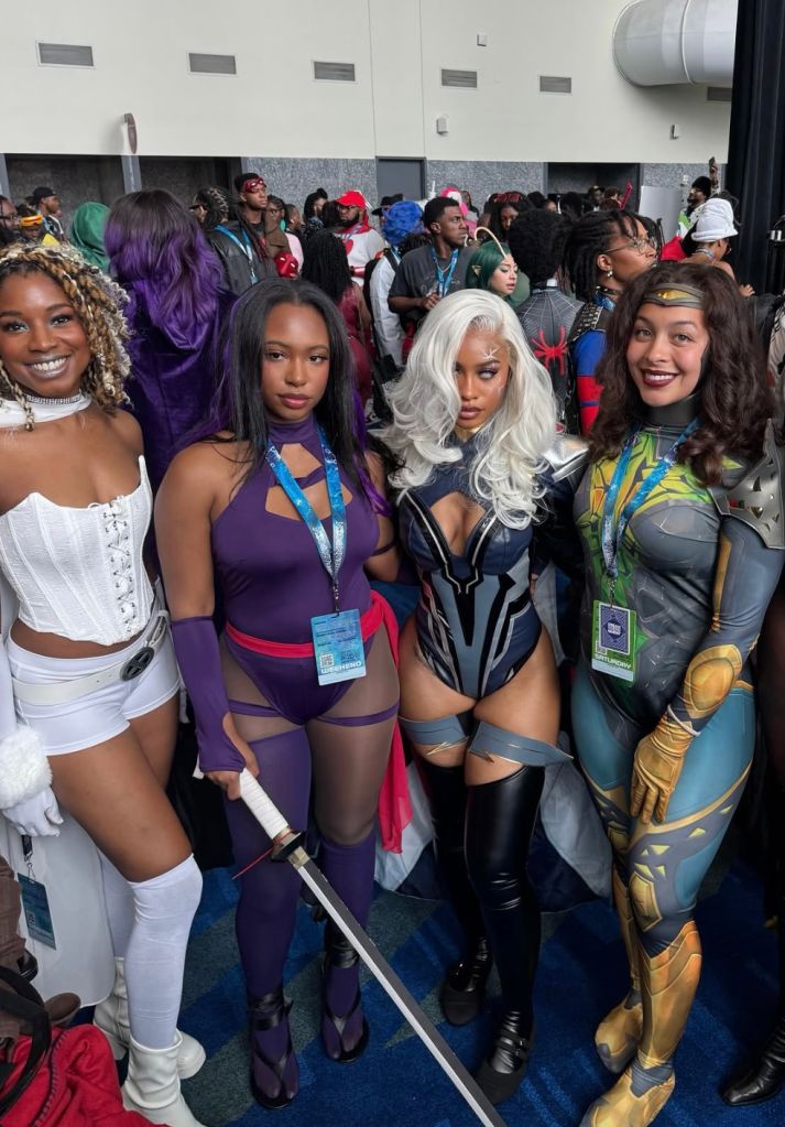 A diverse group of people in colorful superhero-inspired costumes posing together at what appears to be a convention or event.