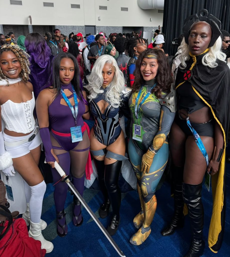 A group of people dressed in colorful, elaborate costumes and superhero-inspired outfits posing together in a convention center hallway.