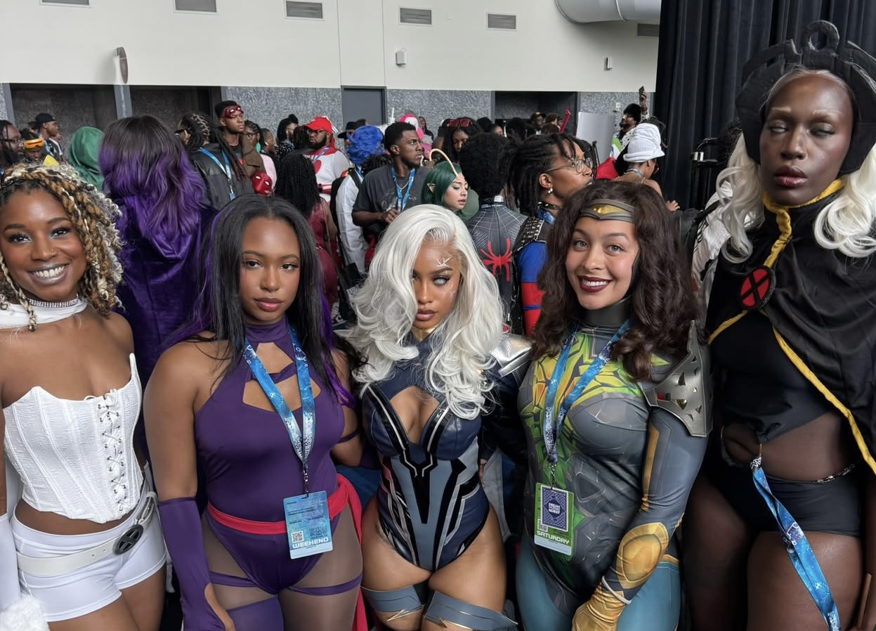 A group of people dressed in colorful, creative superhero and comic book character costumes posing together at what appears to be a comic convention or similar event.
