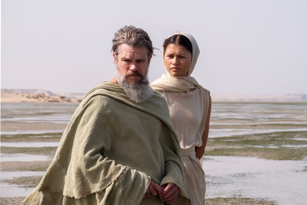Two people, a bearded man and a woman wearing a headscarf, standing on a beach.