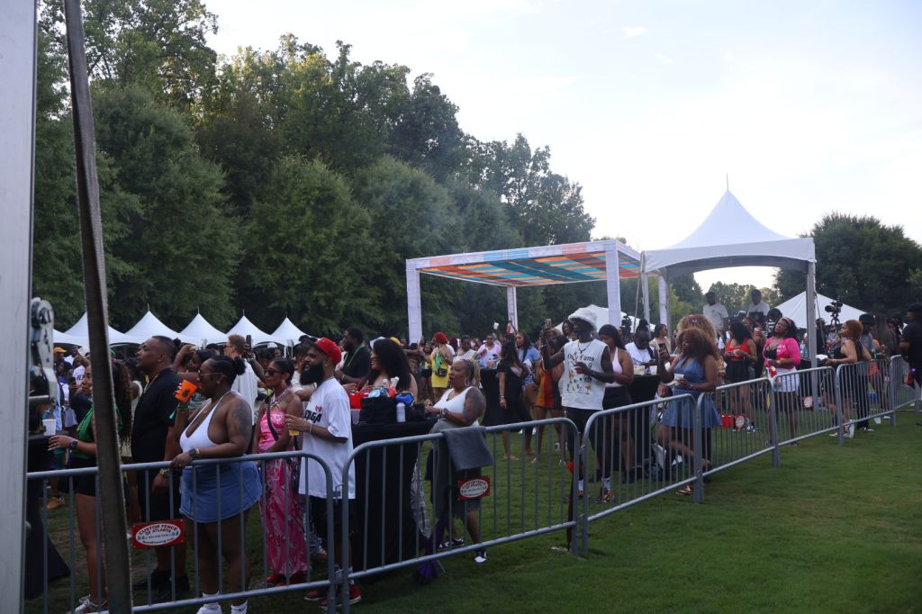A crowded outdoor event with tents, barricades, and a large crowd of people gathered on a grassy field.