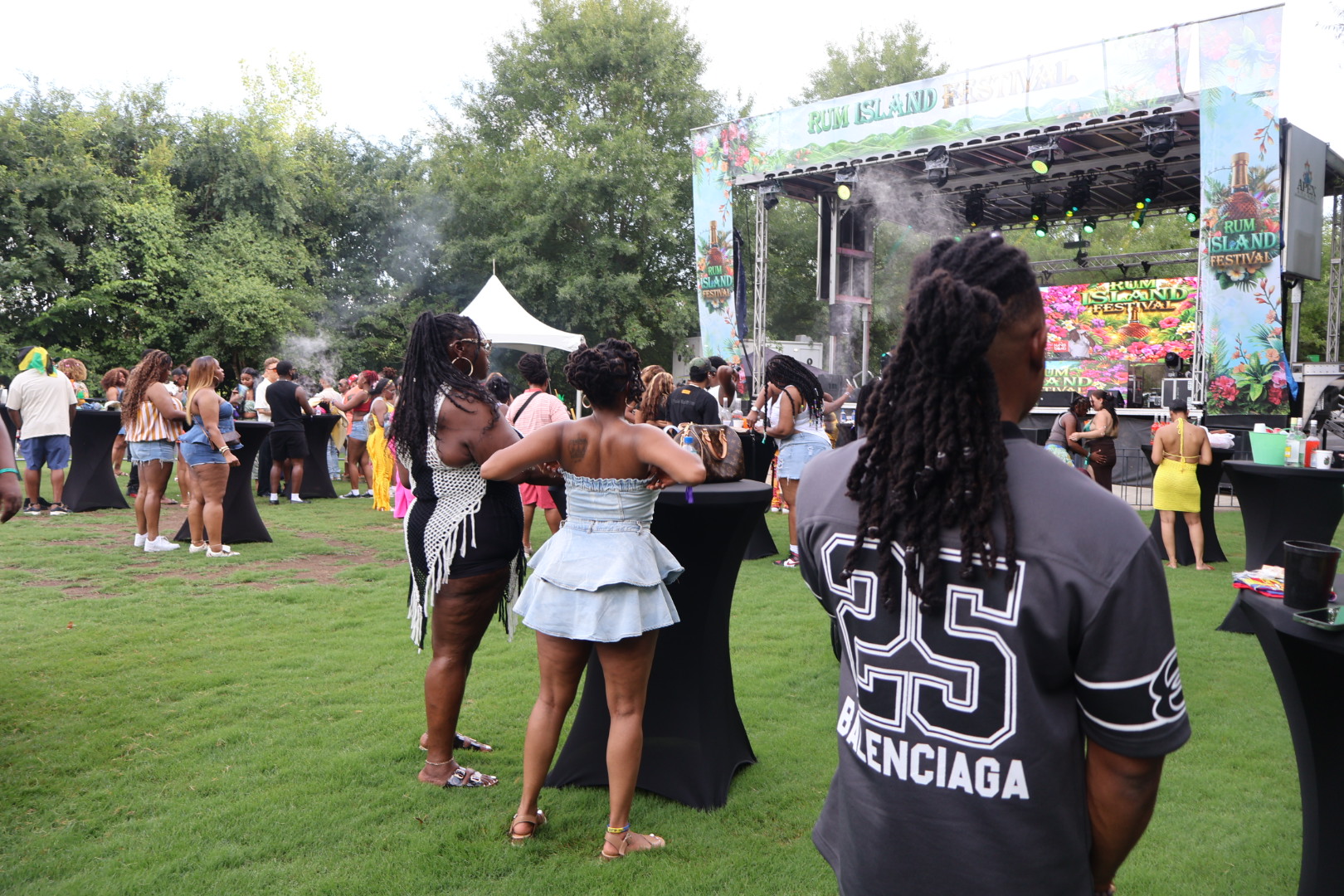 Outdoor music festival with people dancing and enjoying the event. Large stage with "Rum Island Festival" branding visible.