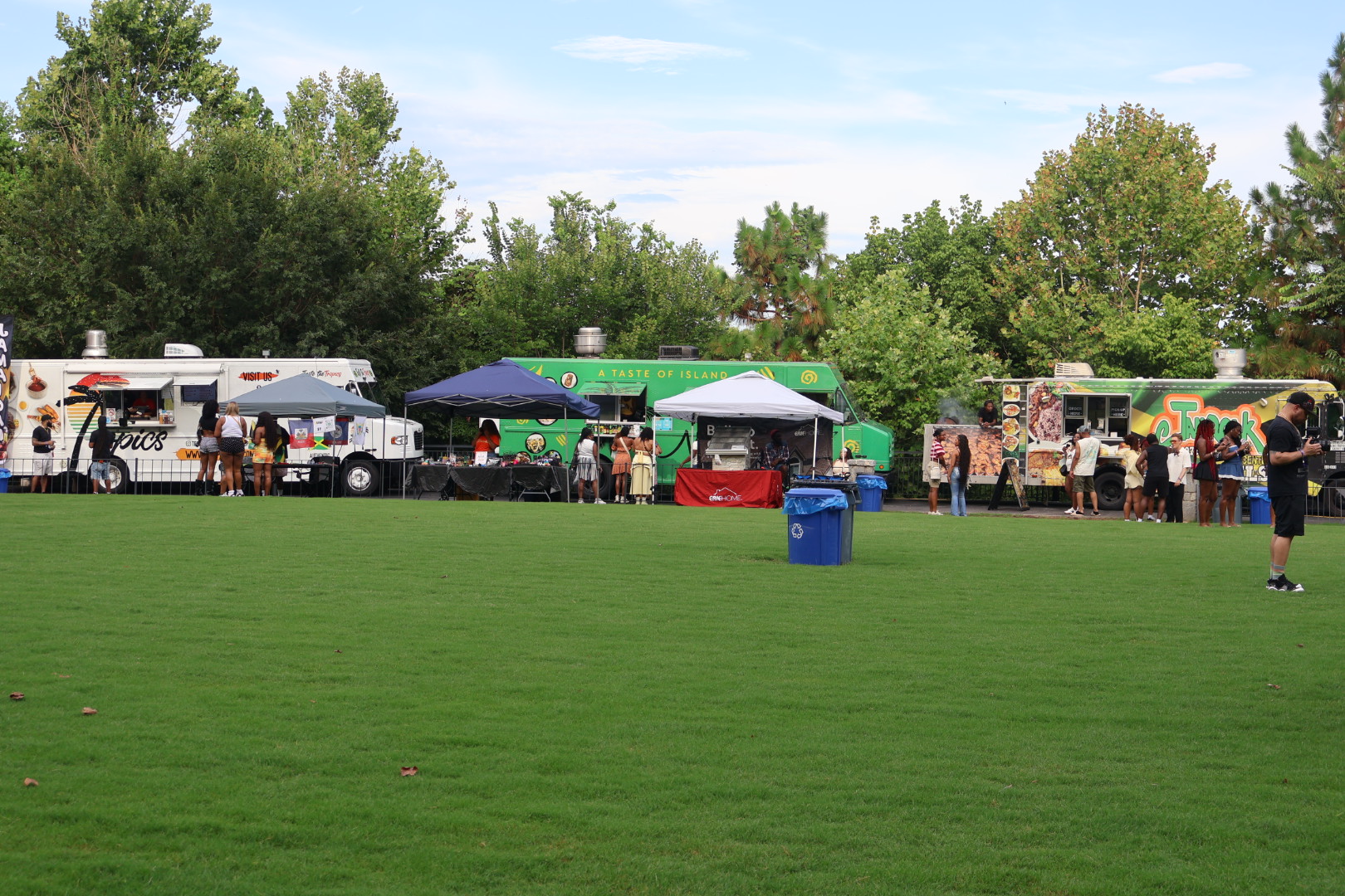 Food trucks and tents set up in a grassy park area with trees in the background.