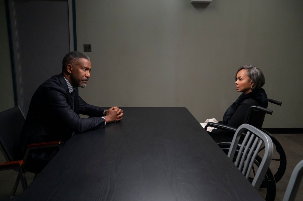 Two people, a man and a woman, sitting at a table in a dimly lit room, engaged in a serious conversation.