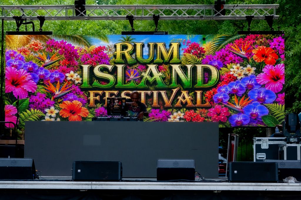 Colorful floral display with "Rum Island Festival" text against a lush green backdrop.