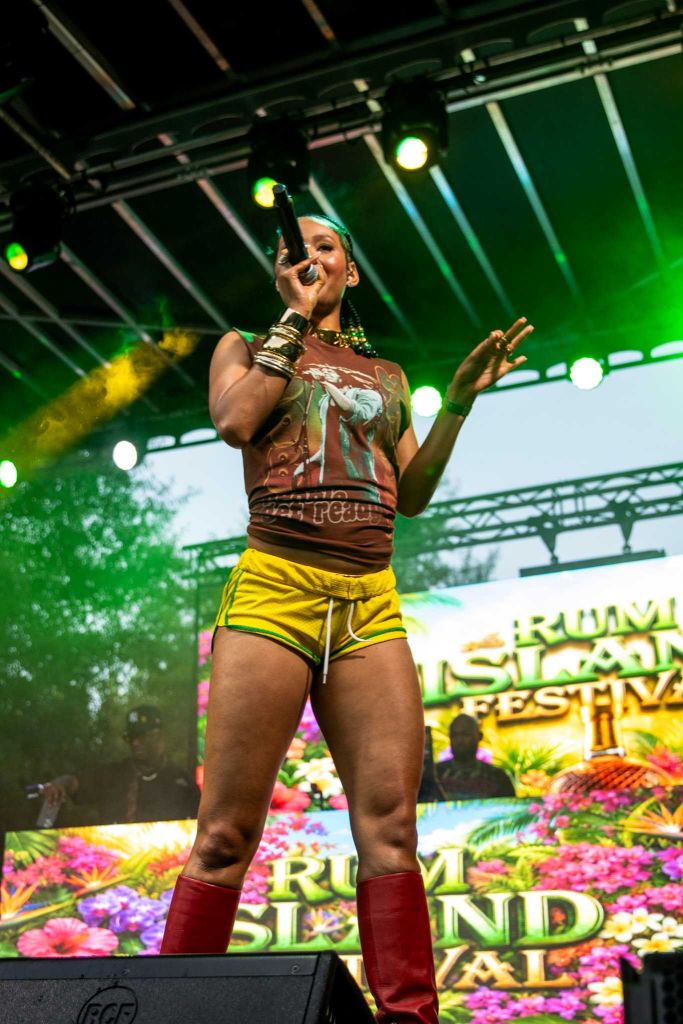 A performer on stage wearing a colorful outfit and accessories, singing into a microphone at the Rum Island Festival.