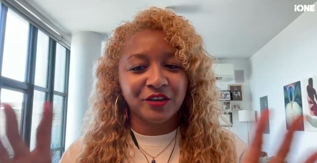 A close-up portrait of a young woman with curly blonde hair and red lipstick, looking directly at the camera with a slight smile.