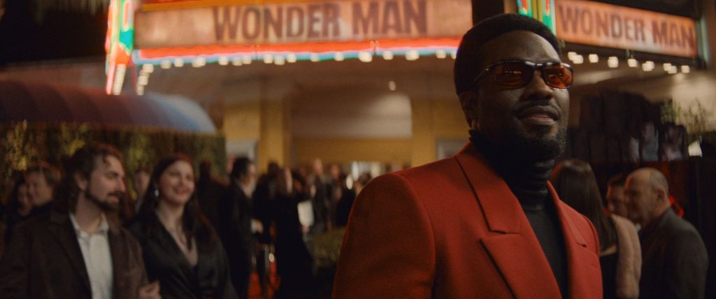 A man in a red suit stands in front of a "Wonder Man" marquee, surrounded by a crowd of people.