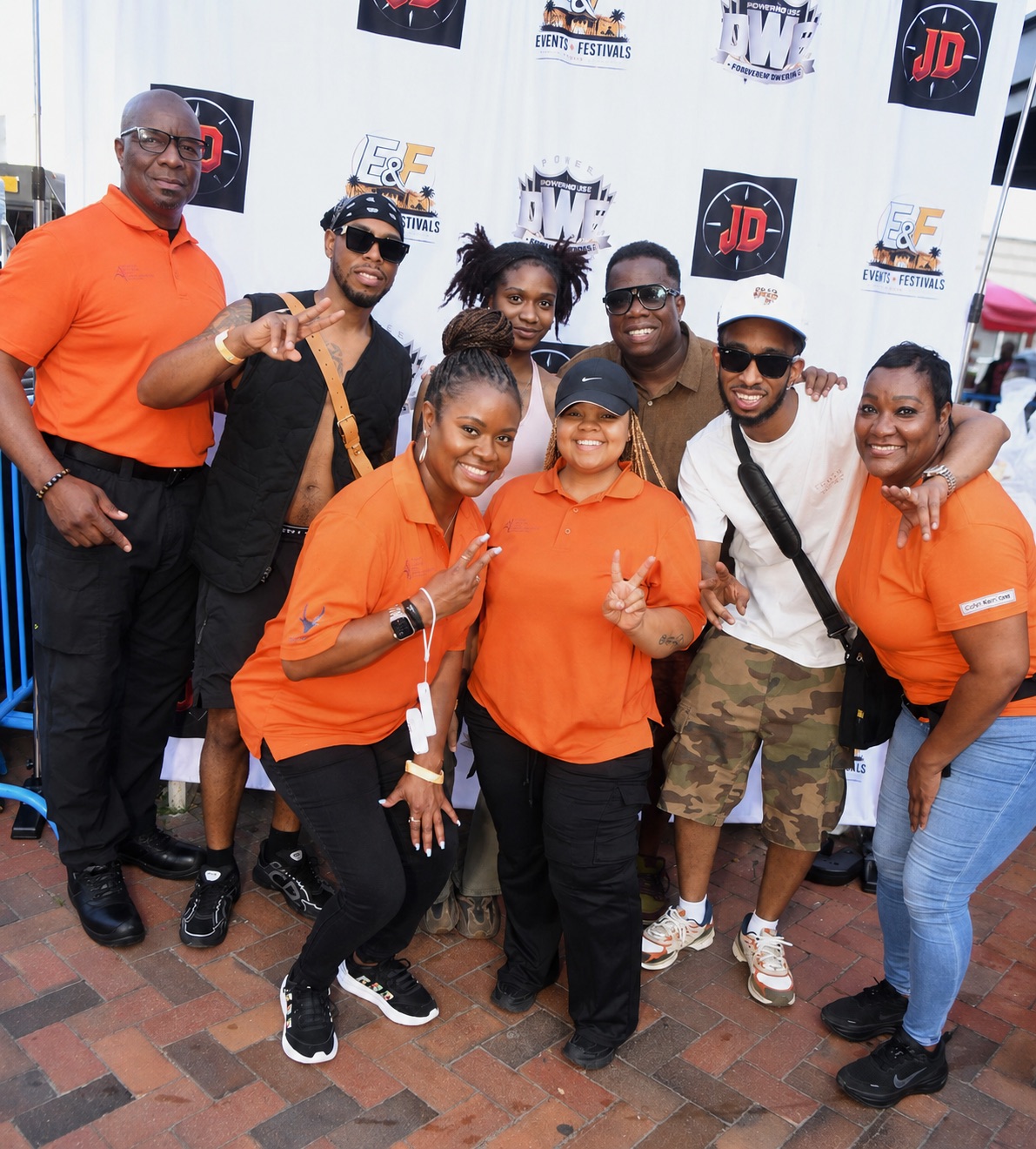 A group of people wearing orange shirts with various event and festival logos, posing together and making peace signs.