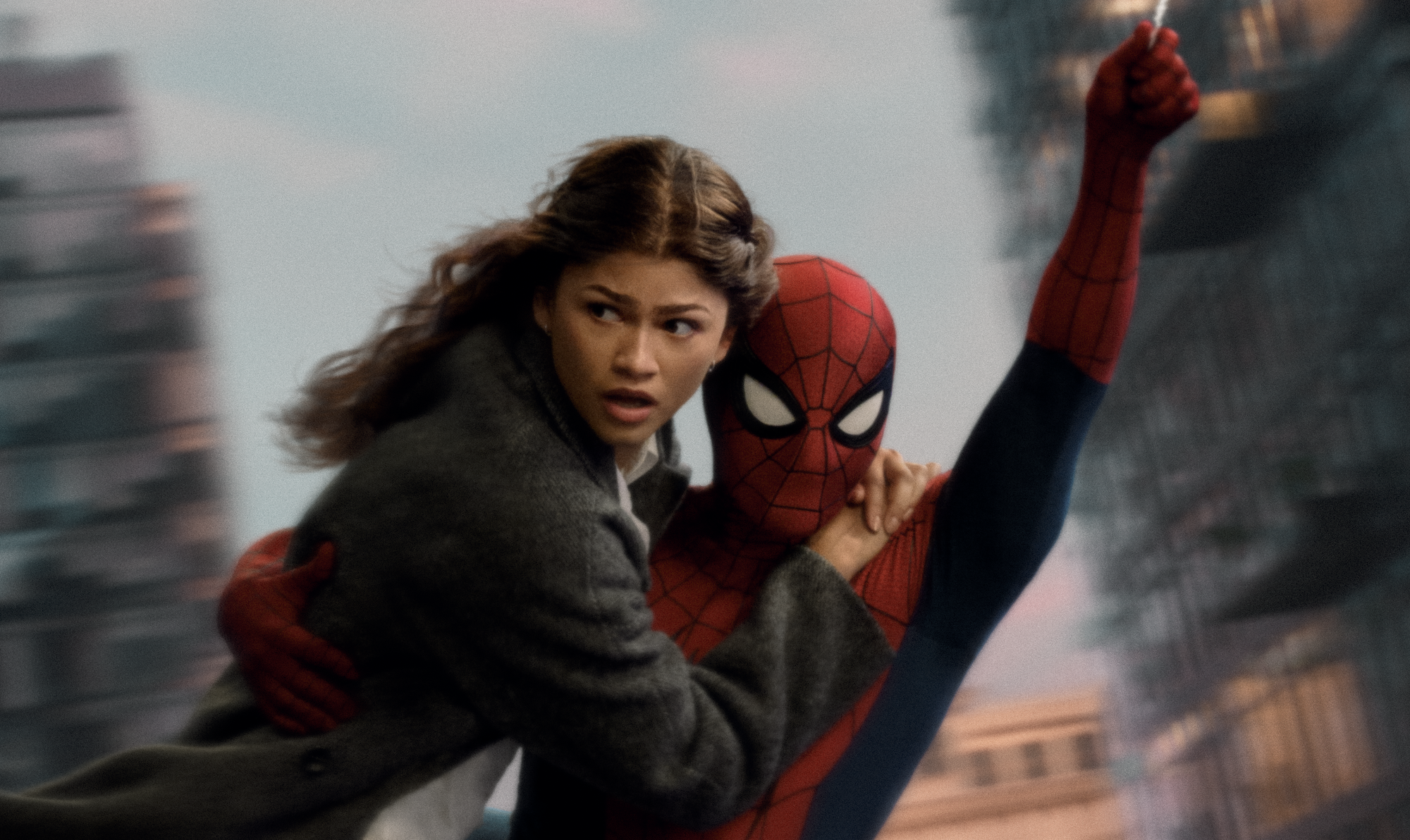 A person in a red and blue Spider-Man costume embracing a woman in a gray coat against a blurred urban backdrop.