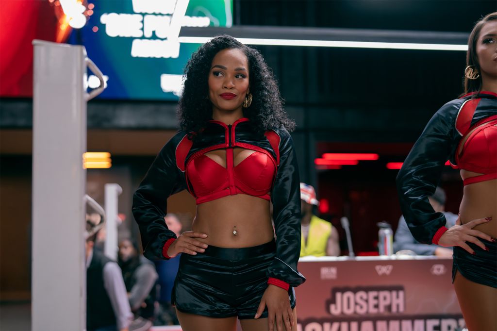 A woman wearing a red crop top and black jacket stands in a setting with neon signs and other people in the background.