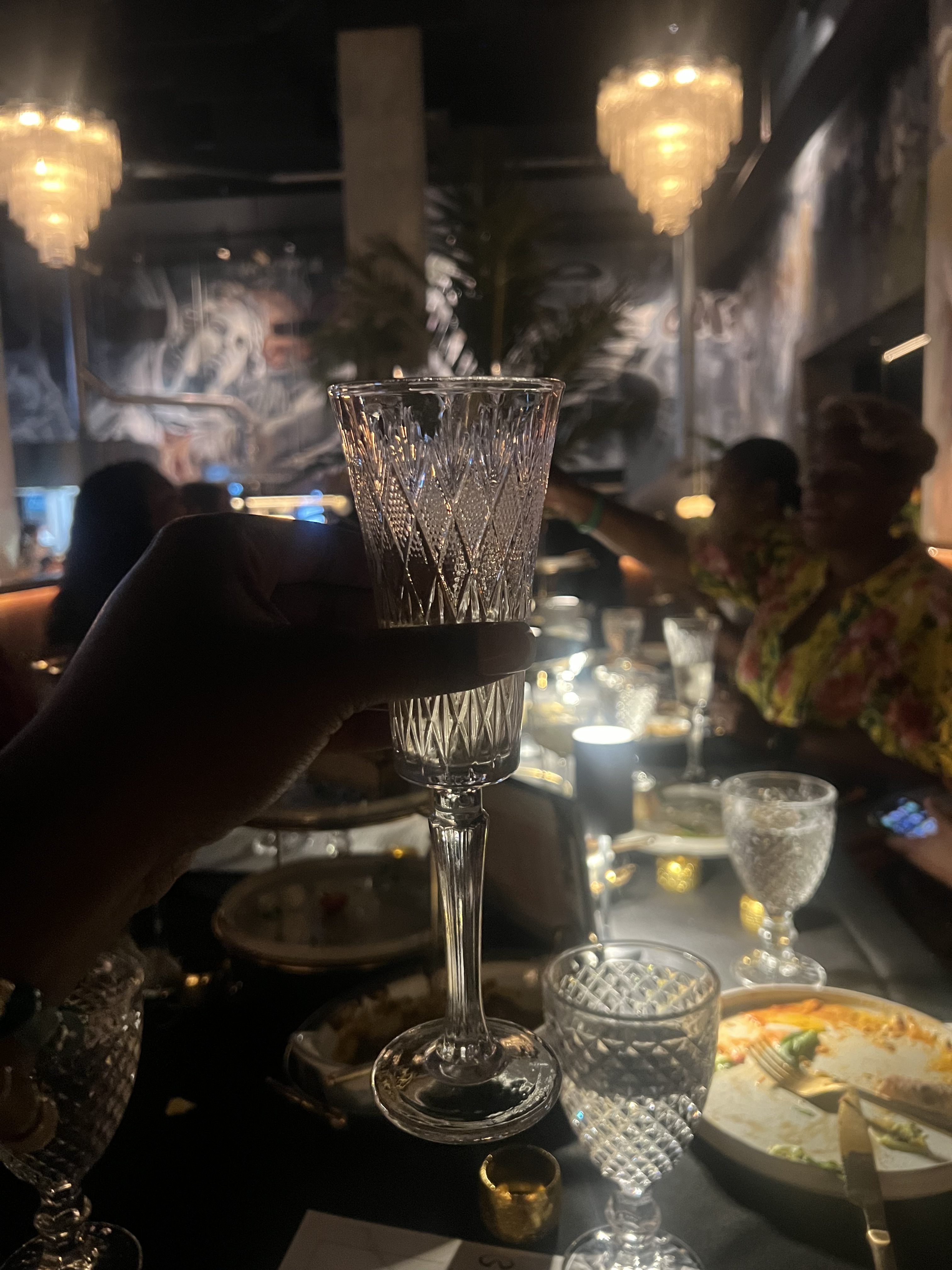 A dimly lit restaurant setting with a crystal wine glass, candles, and other tableware visible on the table.