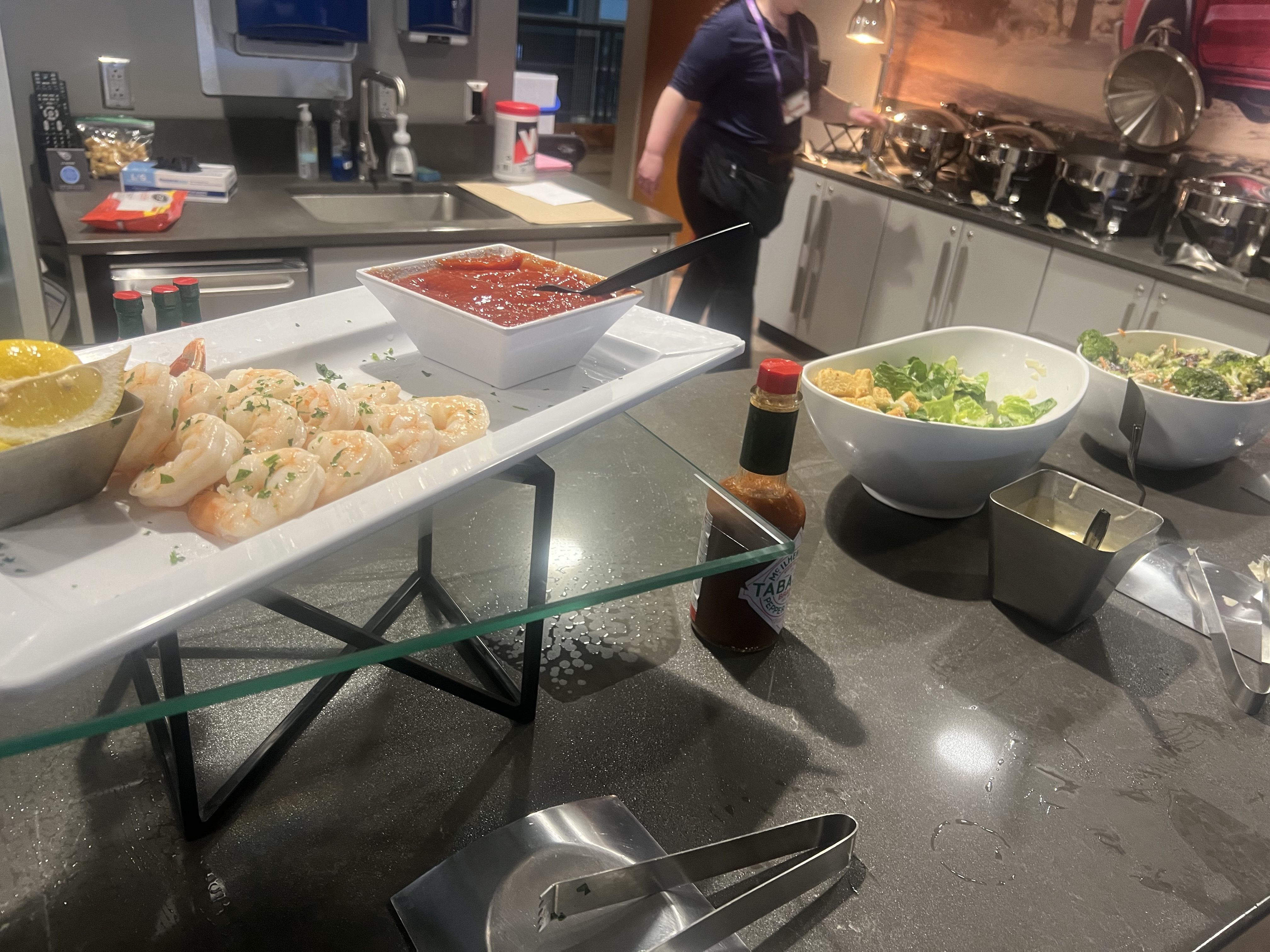 A kitchen counter with various prepared dishes, including shrimp rolls, a red sauce, and a salad. A person is visible in the background.