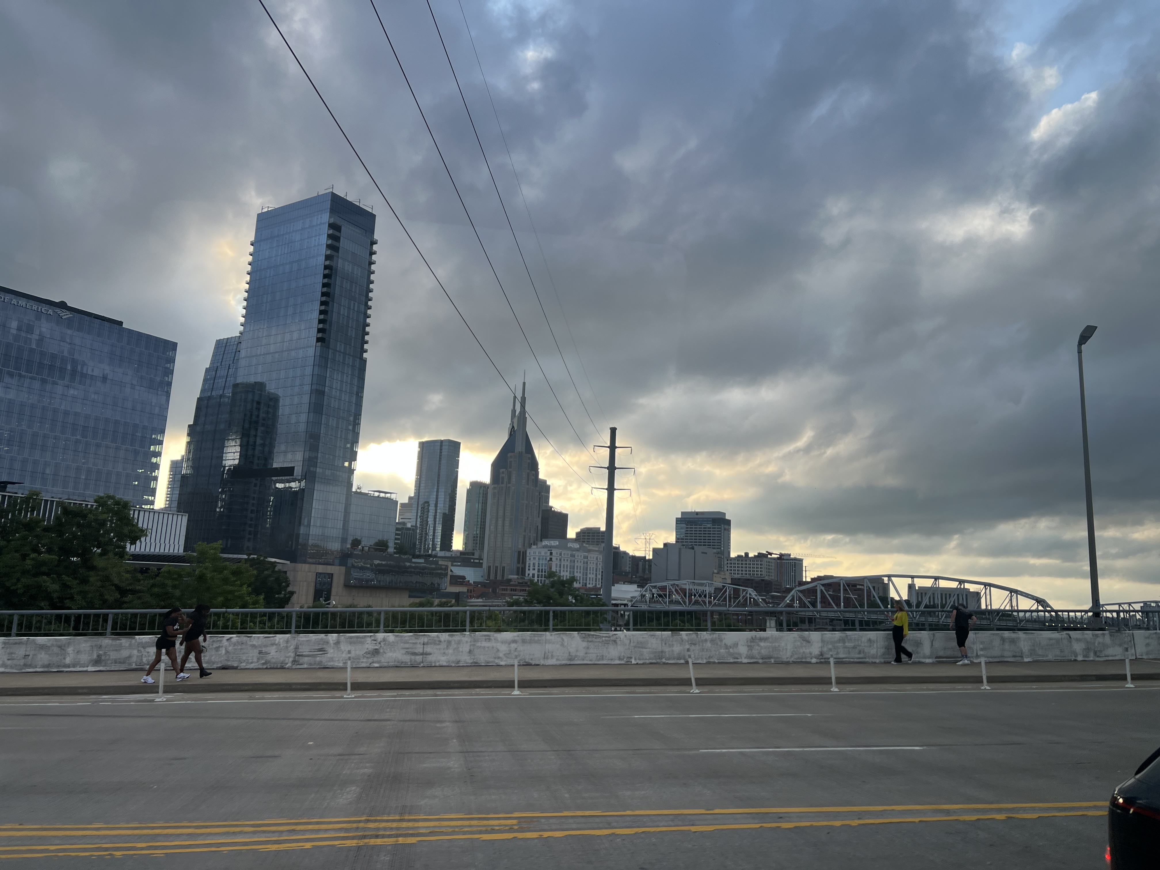 Dramatic cityscape with skyscrapers, bridges, and pedestrians under a cloudy sky in Nashville, Tennessee.