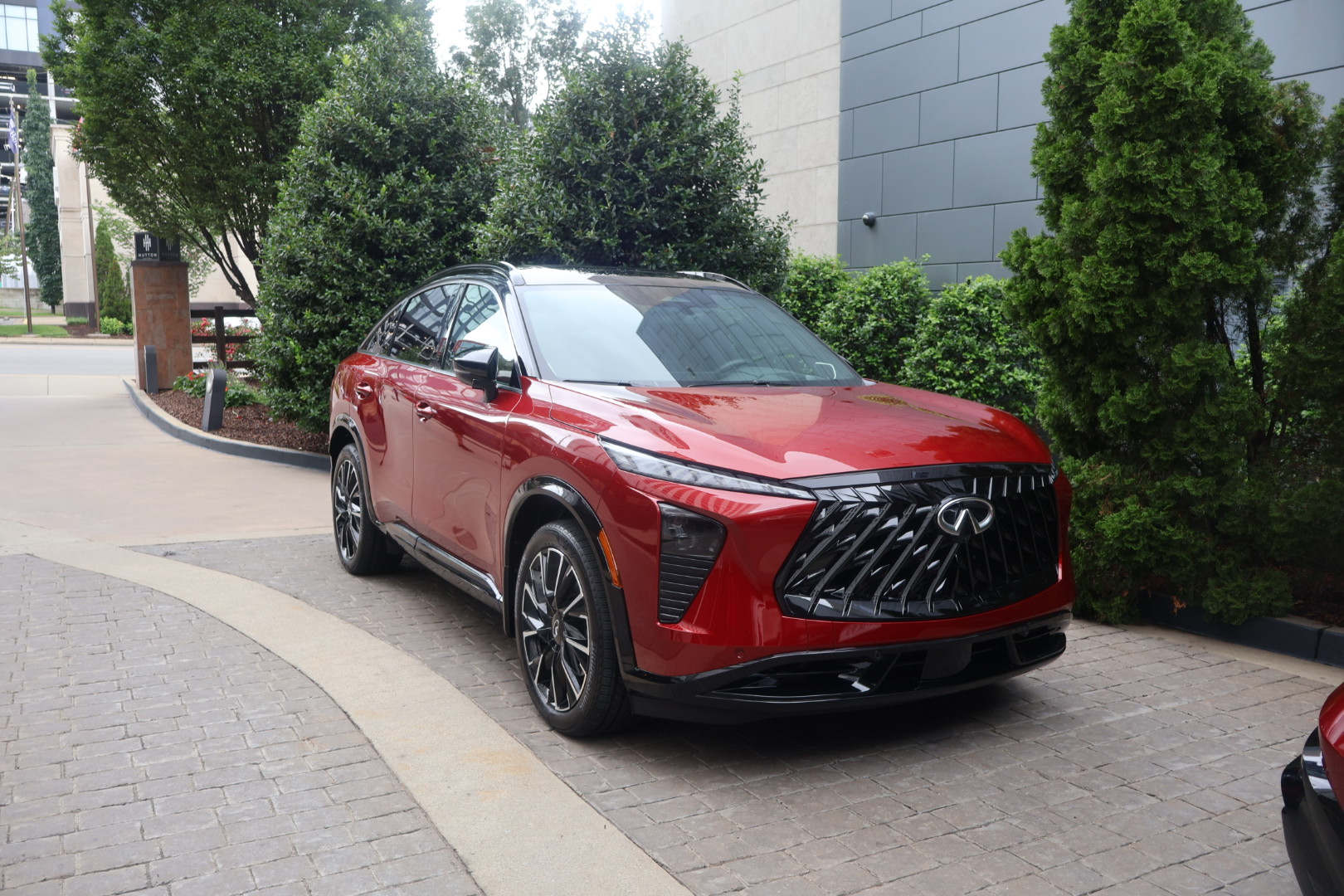 A red luxury SUV with a distinctive front grille design parked in front of a modern building surrounded by trees.