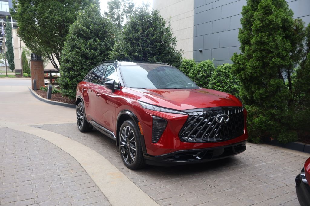 A red luxury SUV with a distinctive front grille design parked in front of a modern building surrounded by trees.
